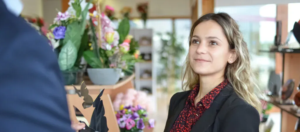 Portrait d'une jeune femme souriante en blazer noir dans un environnement de bureau.
