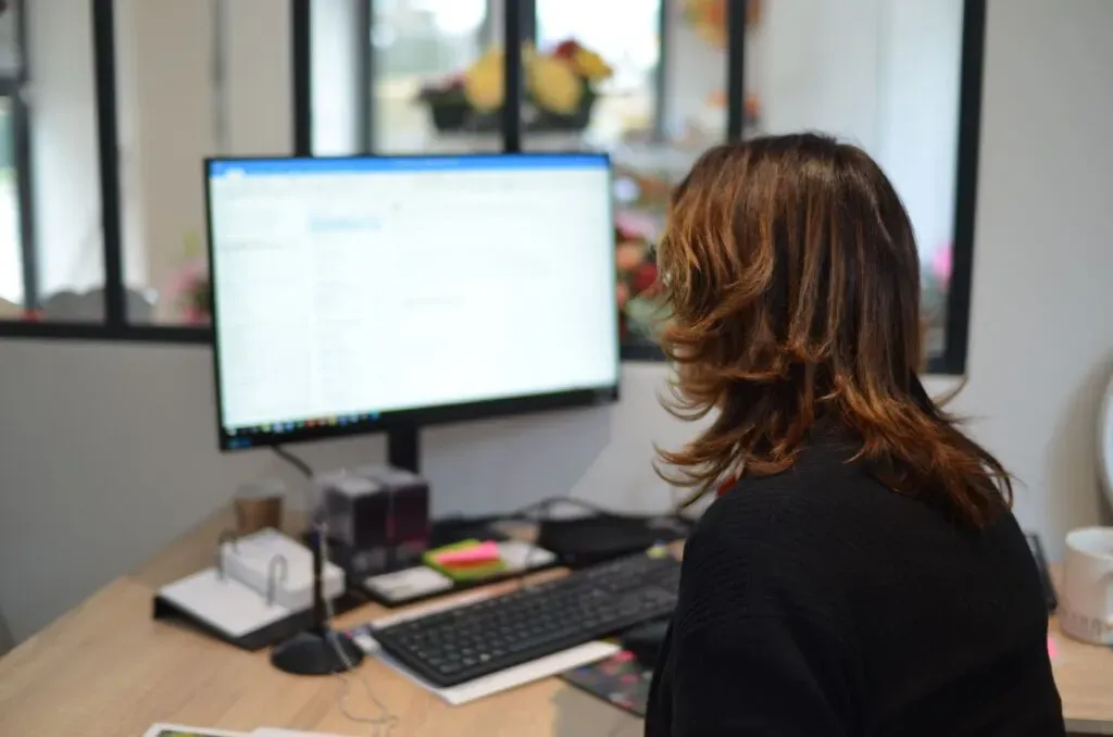 Femme vue de dos travaillant sur ordinateur dans un bureau d'entreprise.