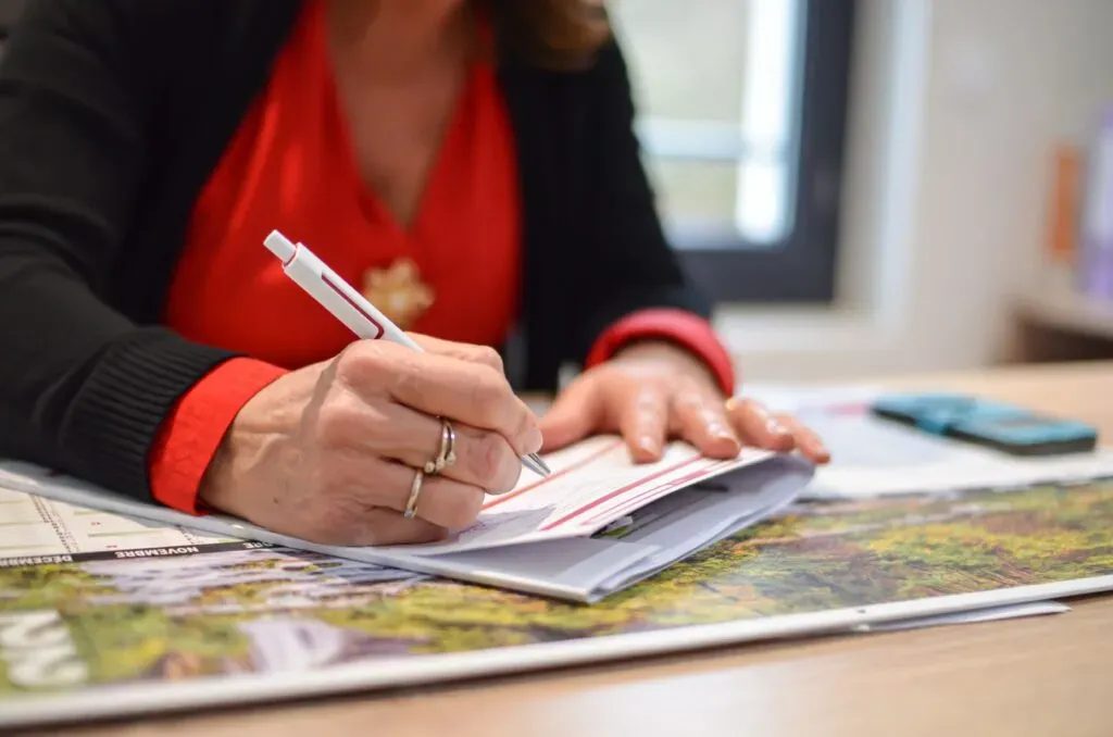 Gros plan sur une personne en chemisier rouge signant un document administratif.