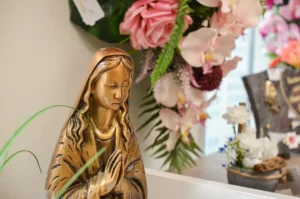 Statuette religieuse de la Vierge Marie en prière devant une gerbe de fleurs artificielles.