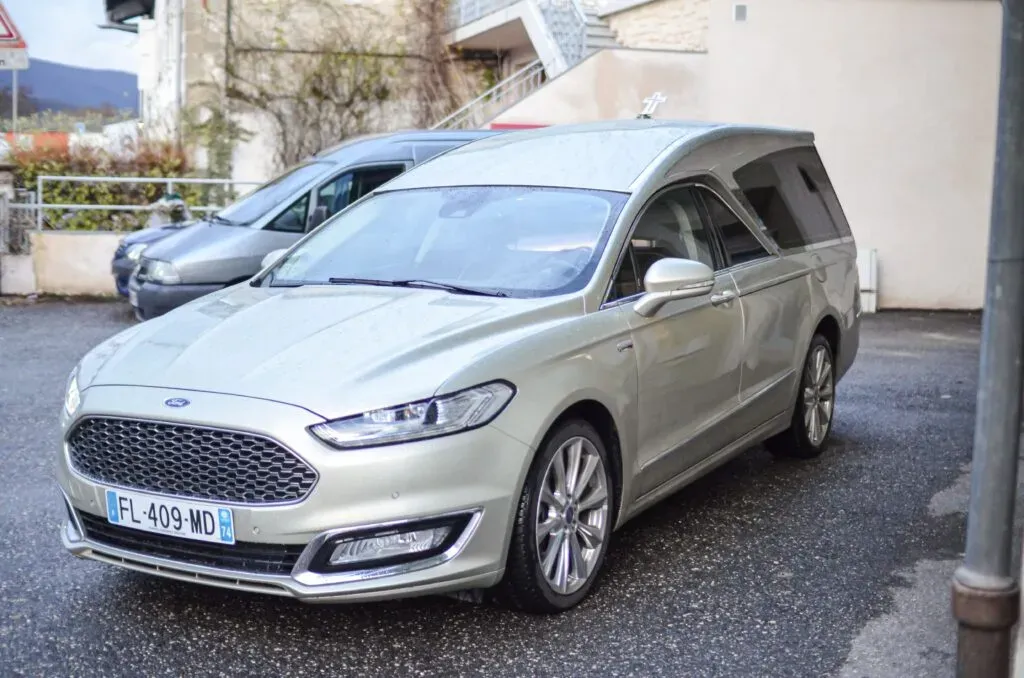 Corbillard Ford Mondeo gris métallisé stationné dans une cour d'immeuble.